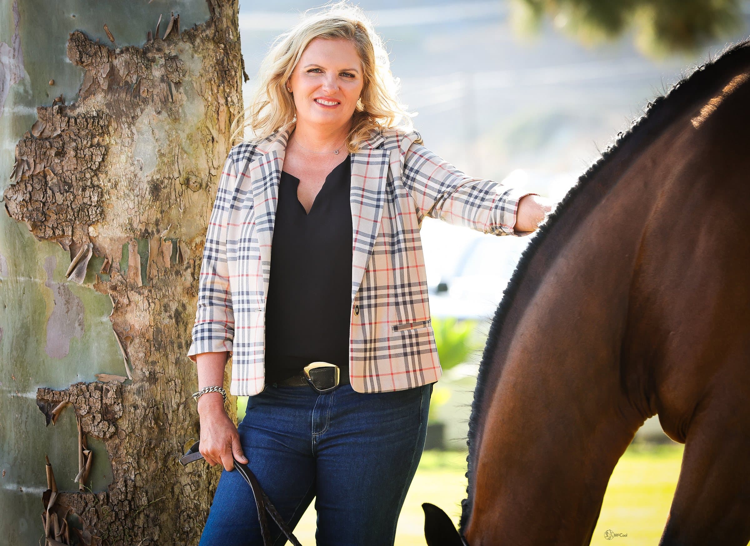Kristin Barreto standing beside a bay horse under a sycamore