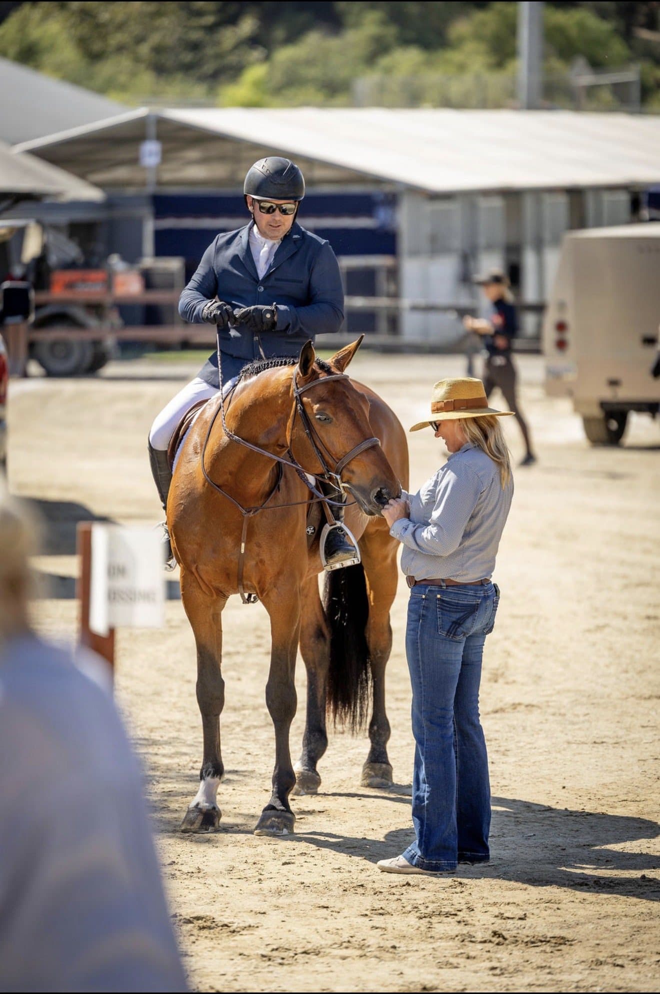 A trainer in a wide-brimmed hat talking with a rider on a chestnut horse